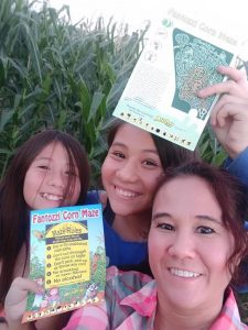 Three woman holding up signs for a corn maze