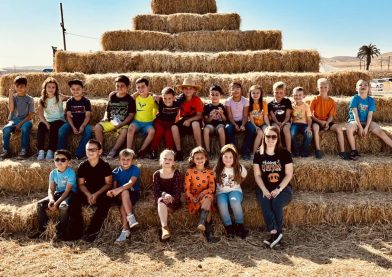 Group of children sitting on stacked hay bales on a sunny day.